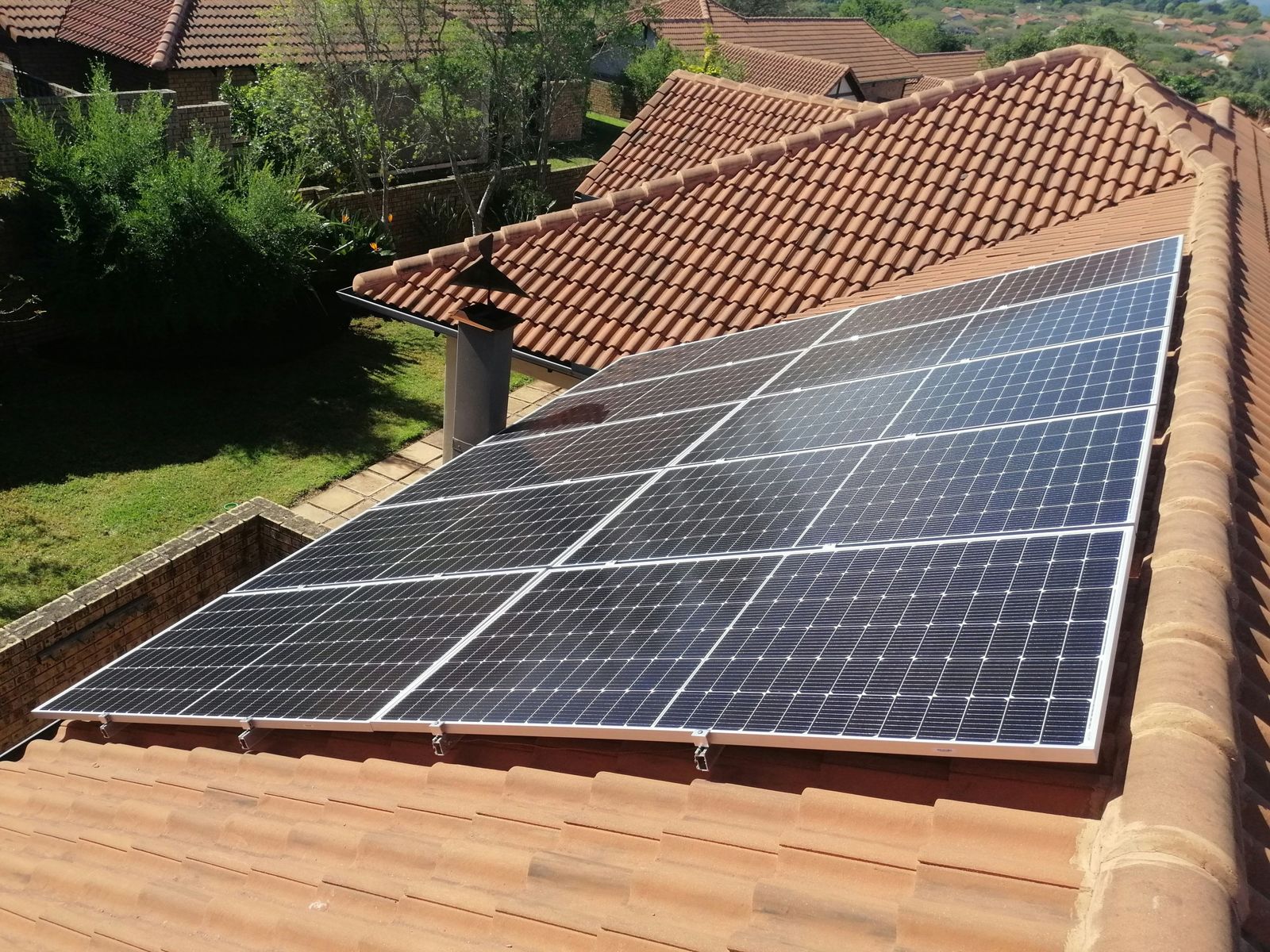 Twelve-panel array on a clay tile roof beside a garden